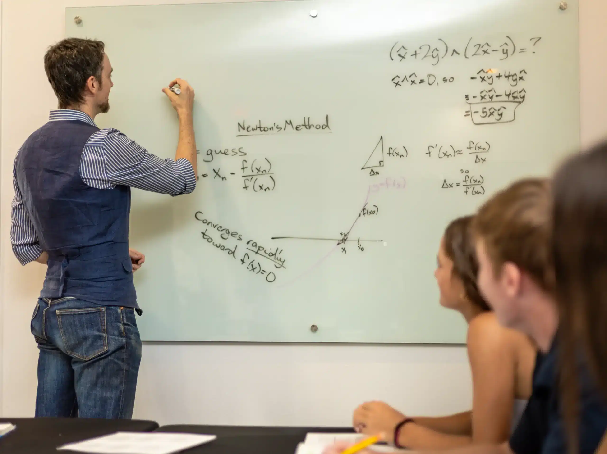 Teacher explaining math equations on whiteboard to students