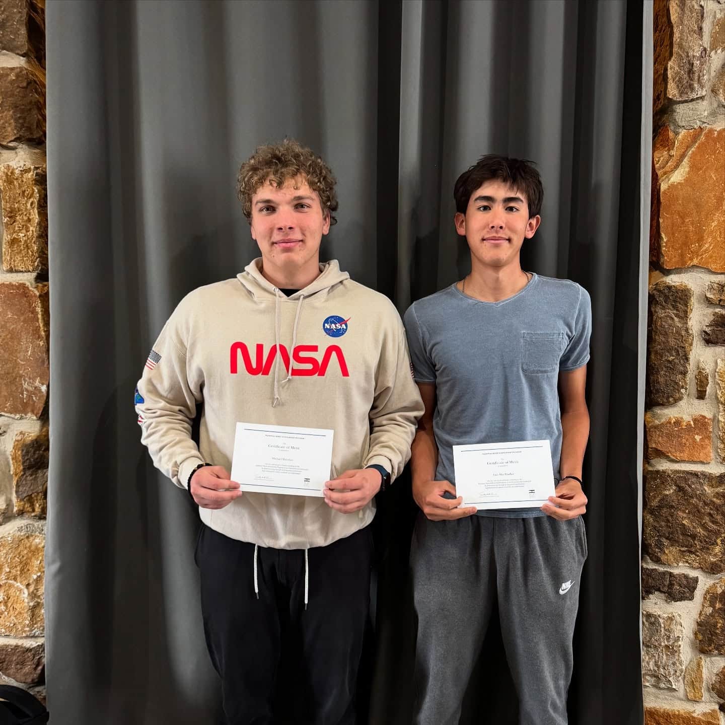Two students holding achievement certificates indoors